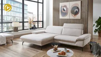 Modernes Wohnzimmer mit großem hellbeigem Ecksofa auf Holzfußboden, verstellbaren Armlehnen und schwarzen Metallfüßen.